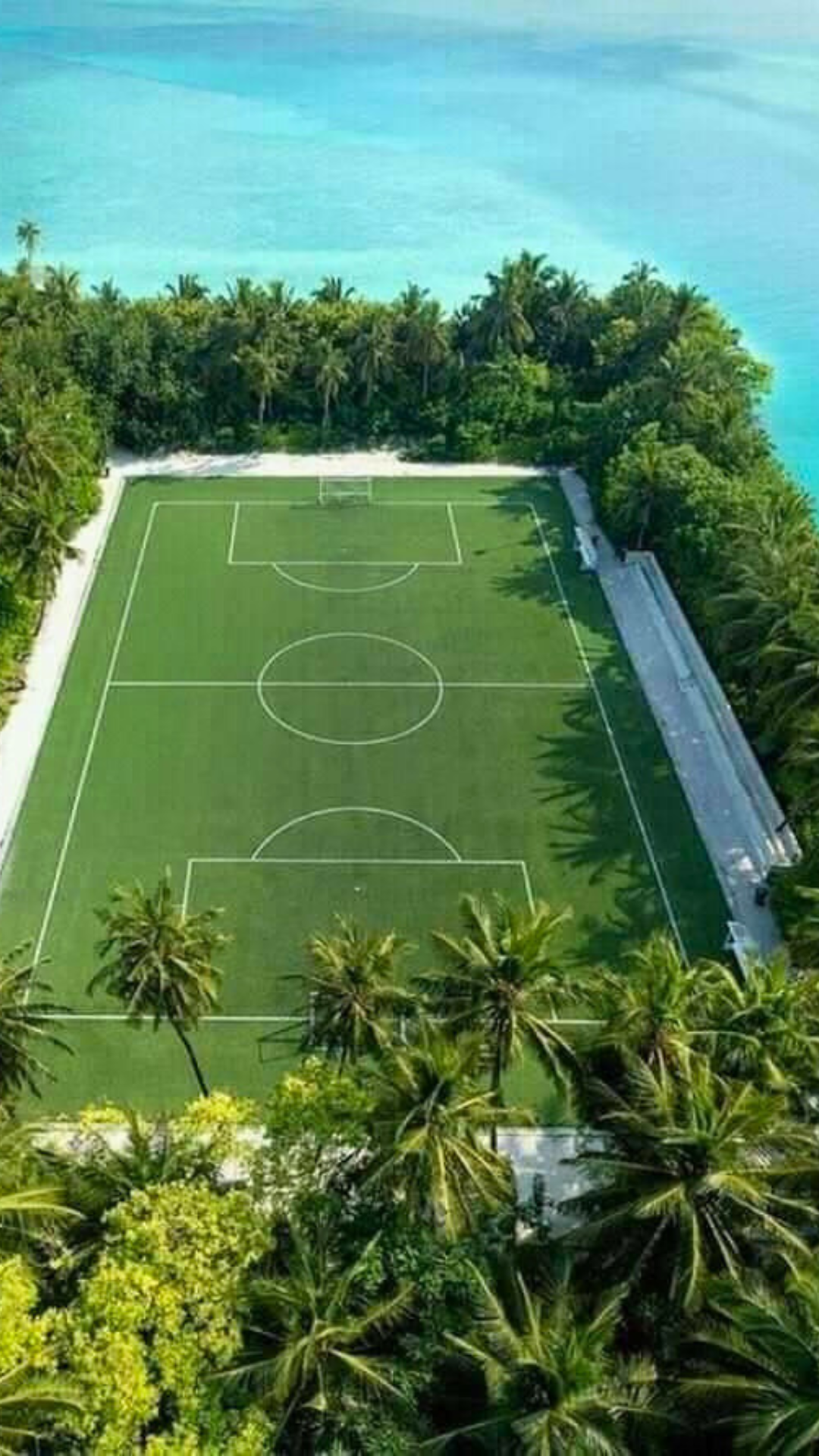 Aerial view of a soccer pitch surrounded by palm trees and turquoise ocean